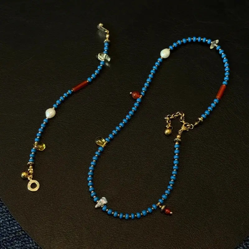 Flatlay of the handmade Blue beaded necklace on a black background, showcasing the mix of blue glass beads, natural stones, freshwater pearls, and black hematite.