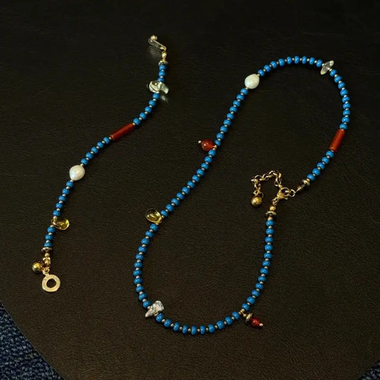 Flatlay of the handmade Blue beaded necklace on a black background, showcasing the mix of blue glass beads, natural stones, freshwater pearls, and black hematite.