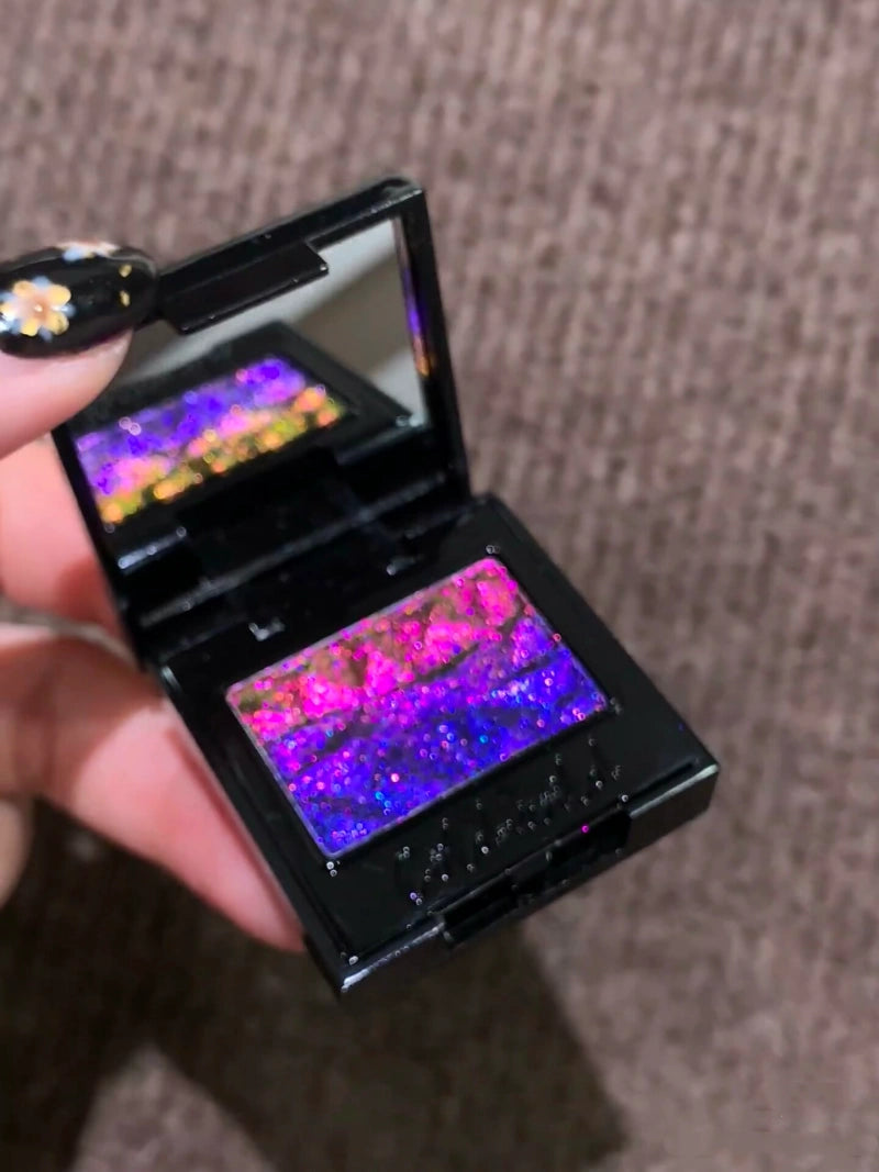 Side view of the Holographic Shift eyeshadow compact, held at an angle to demonstrate the dramatic color shift from purple to blue as light hits the surface.